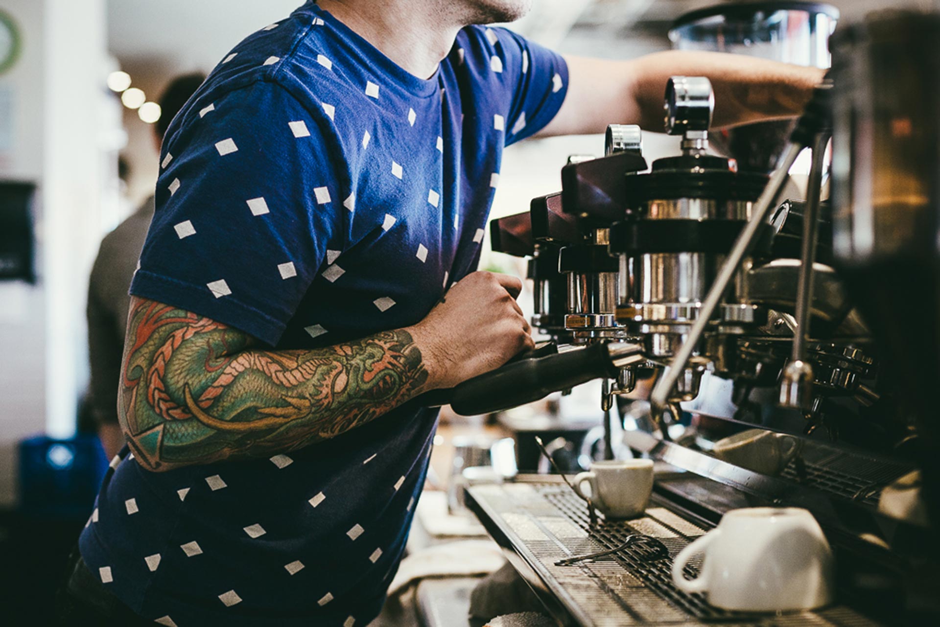 man with arm tattoo making a espresso at the village café